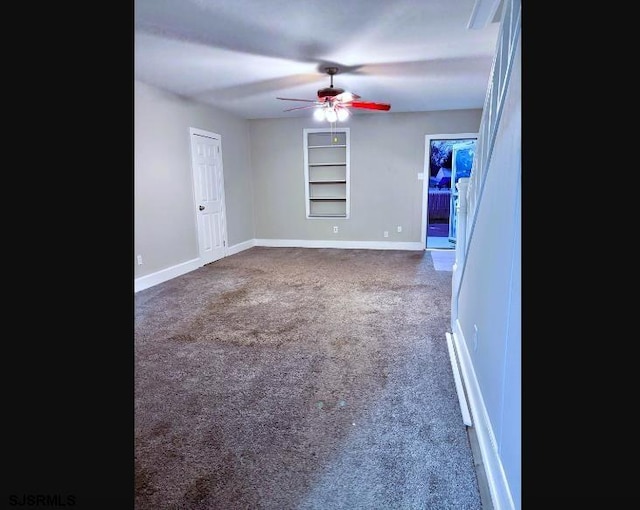 empty room featuring built in shelves, dark colored carpet, ceiling fan, and baseboards
