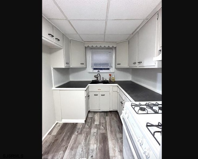 kitchen featuring dark wood-style flooring, white gas stove, dark countertops, white cabinetry, and a sink