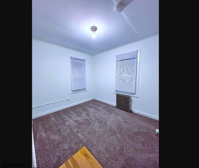 spare room featuring baseboards, dark carpet, and radiator heating unit