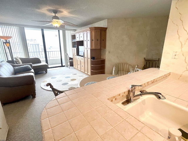 kitchen with tile counters, light colored carpet, a ceiling fan, a sink, and a textured ceiling