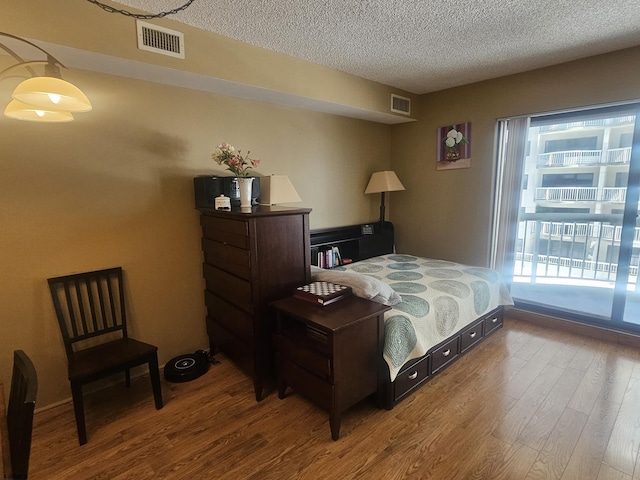 bedroom with visible vents, a textured ceiling, and wood finished floors