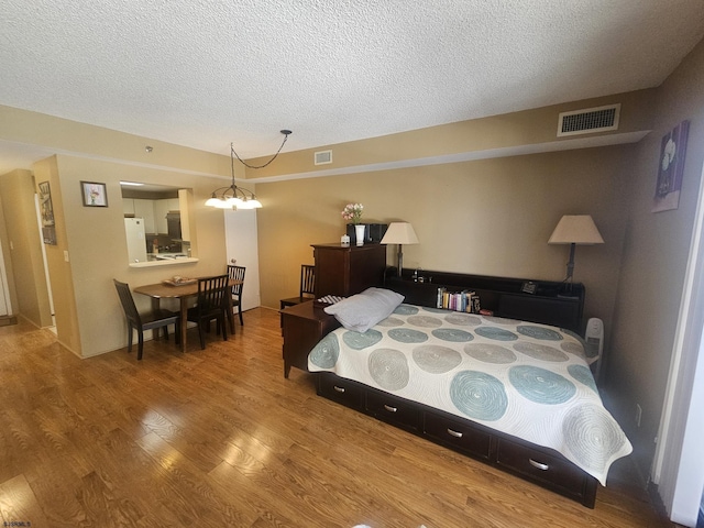 bedroom featuring freestanding refrigerator, visible vents, a textured ceiling, and wood finished floors