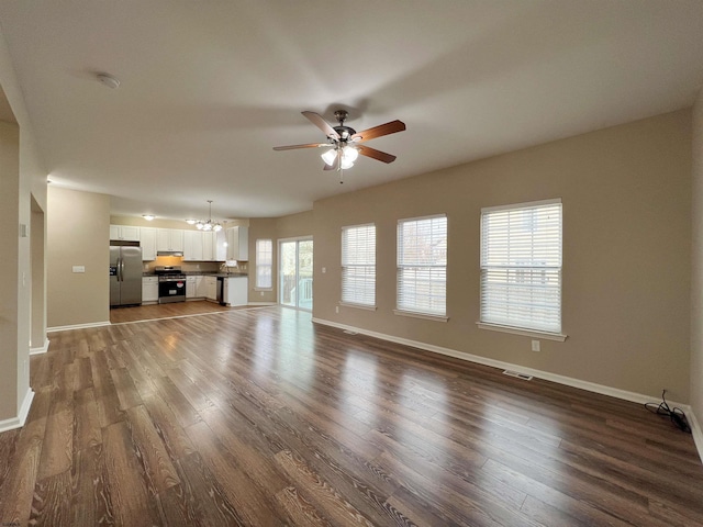 unfurnished living room featuring ceiling fan with notable chandelier, dark wood finished floors, and baseboards