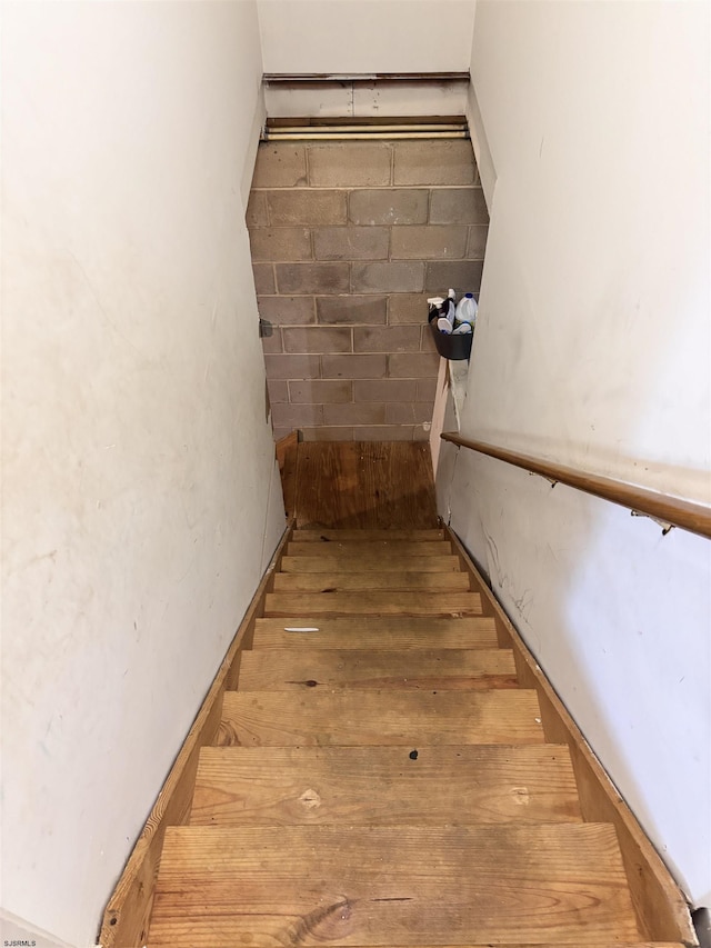 stairway with wood finished floors and concrete block wall