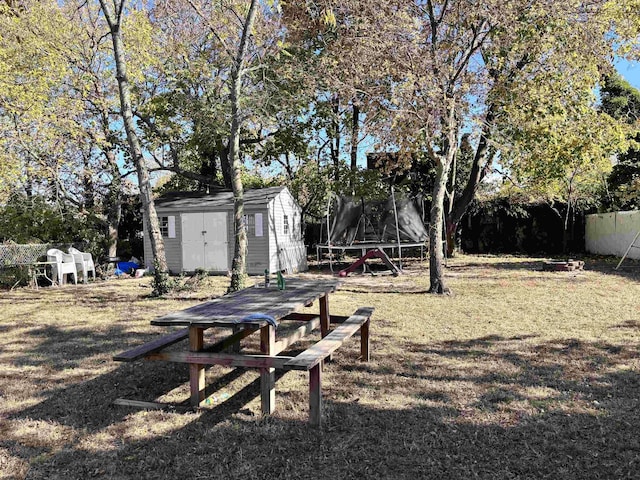 view of yard with a trampoline, an outbuilding, fence, and a storage unit