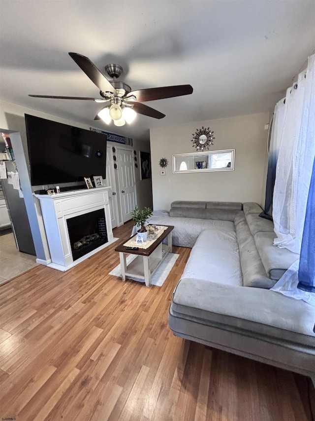 living area with a ceiling fan, a fireplace, and light wood-style flooring