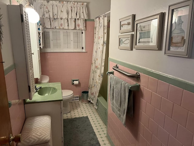 bathroom featuring toilet, a wainscoted wall, shower / bath combination with curtain, vanity, and tile walls