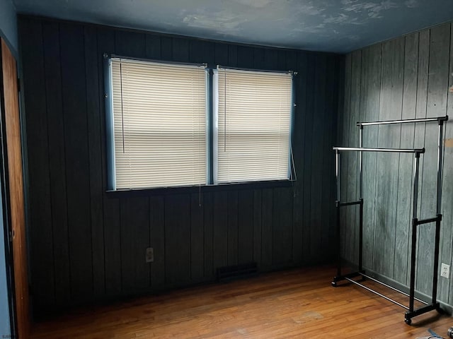 empty room with visible vents, light wood-style flooring, and wooden walls