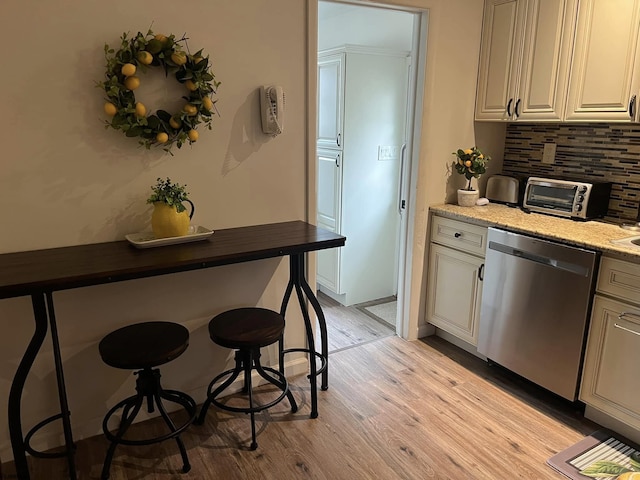 kitchen with light stone counters, light wood-style flooring, a toaster, dishwasher, and tasteful backsplash