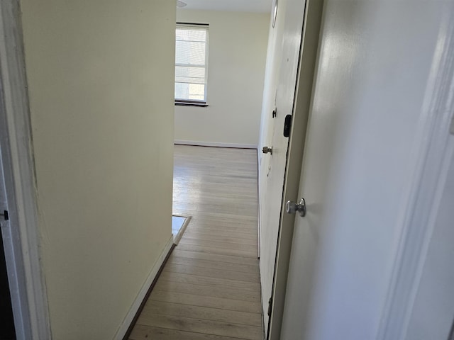 hallway featuring light wood finished floors and baseboards