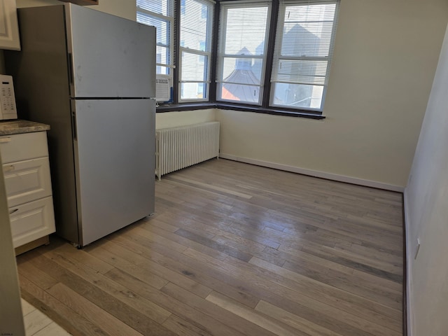 kitchen with white appliances, radiator heating unit, light wood-type flooring, and white cabinets