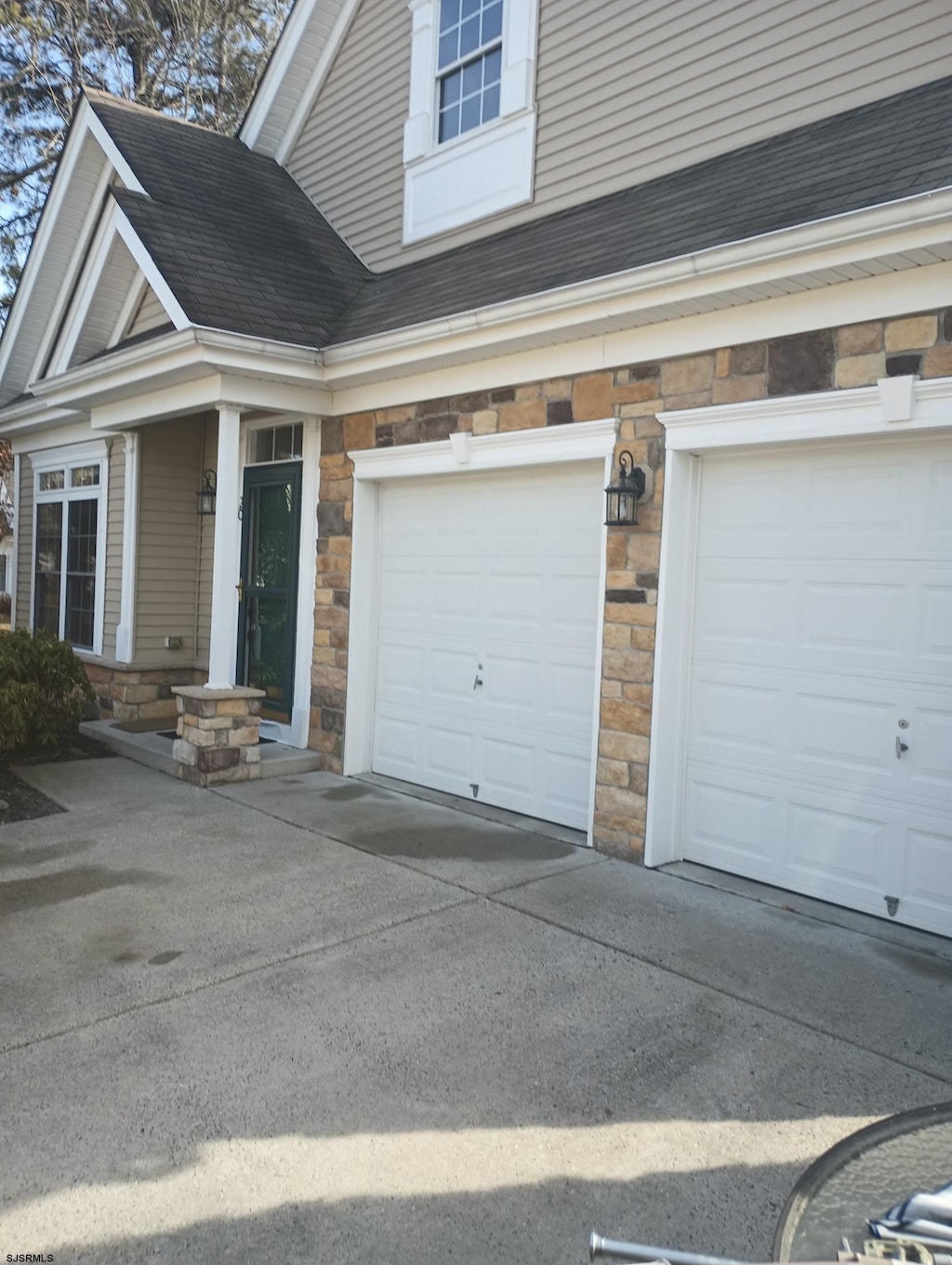 exterior space with stone siding, roof with shingles, and driveway