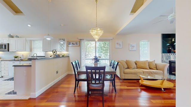 dining room featuring ceiling fan with notable chandelier, lofted ceiling, a tiled fireplace, and wood finished floors