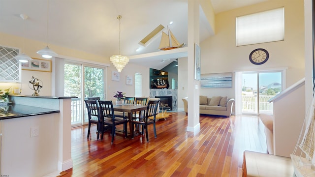 dining area with high vaulted ceiling, a tile fireplace, plenty of natural light, and wood finished floors