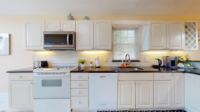 kitchen featuring dark countertops, white appliances, white cabinetry, and a sink