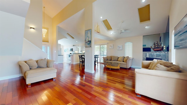 living area featuring high vaulted ceiling, wood finished floors, a ceiling fan, and baseboards