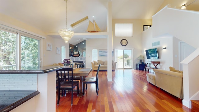 dining area with high vaulted ceiling, a notable chandelier, wood finished floors, visible vents, and a tiled fireplace