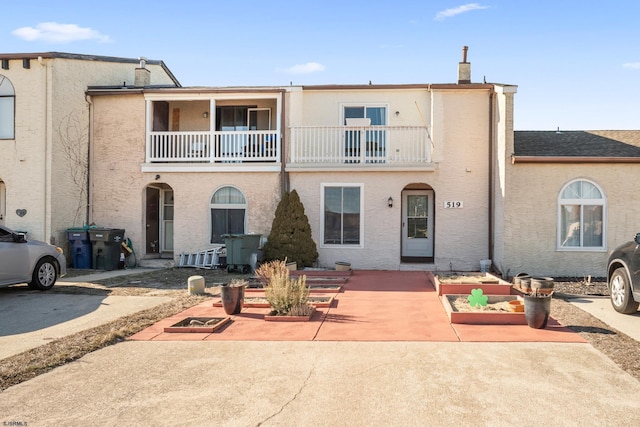 view of front of home featuring a patio, a chimney, a balcony, and stucco siding