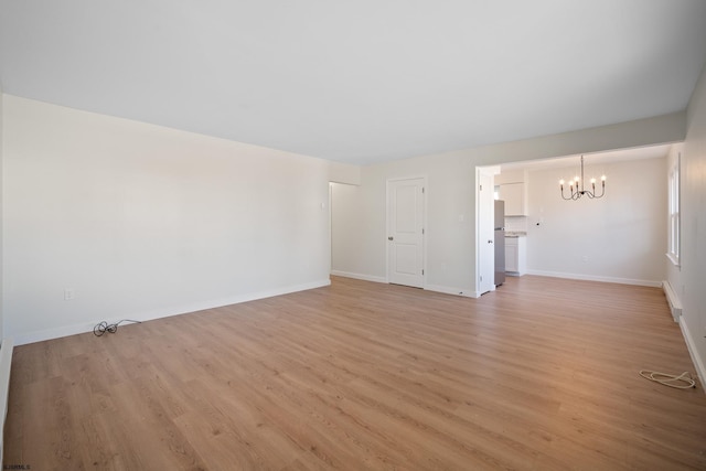 spare room with a chandelier, baseboards, and light wood-style floors