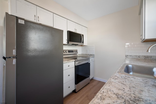 kitchen with stainless steel appliances, decorative backsplash, white cabinetry, a sink, and light wood-type flooring