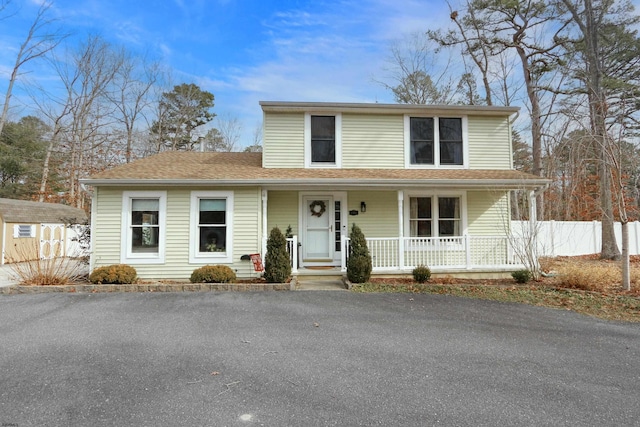 traditional home featuring an outbuilding, roof with shingles, covered porch, a storage shed, and fence