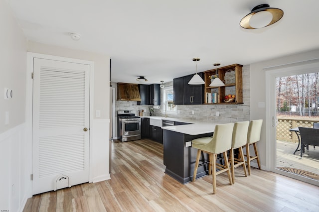 kitchen with stainless steel gas stove, a peninsula, light countertops, a kitchen bar, and open shelves