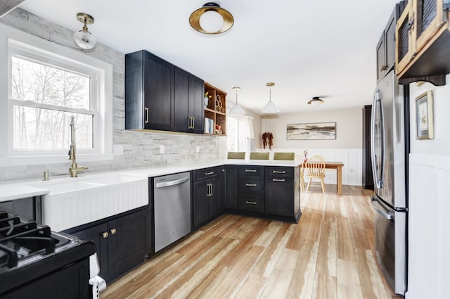 kitchen with a peninsula, stainless steel appliances, hanging light fixtures, light countertops, and open shelves