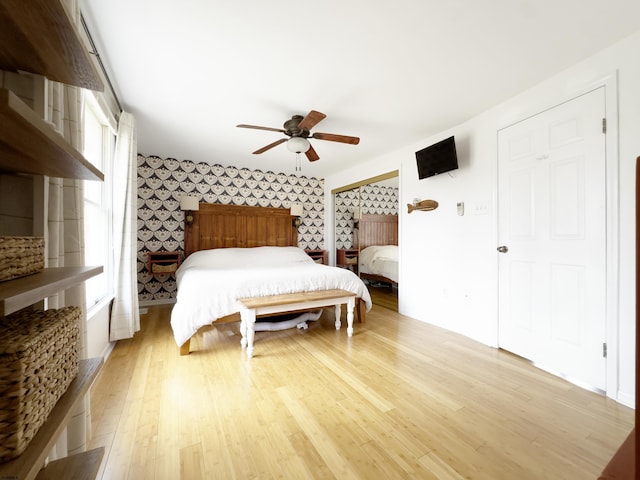 bedroom with light wood-style floors, wallpapered walls, and a ceiling fan