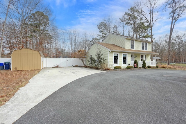 view of side of property featuring covered porch, a gate, fence, a shed, and driveway