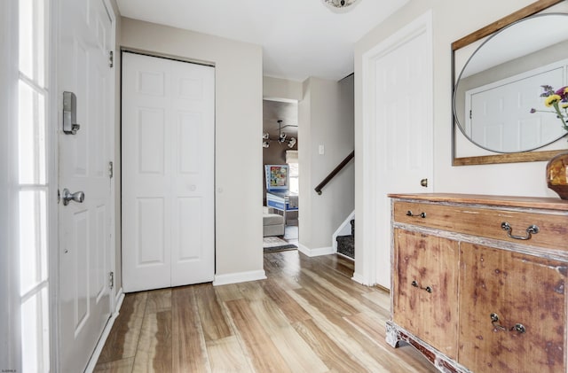 foyer entrance with stairway, light wood-style flooring, and baseboards