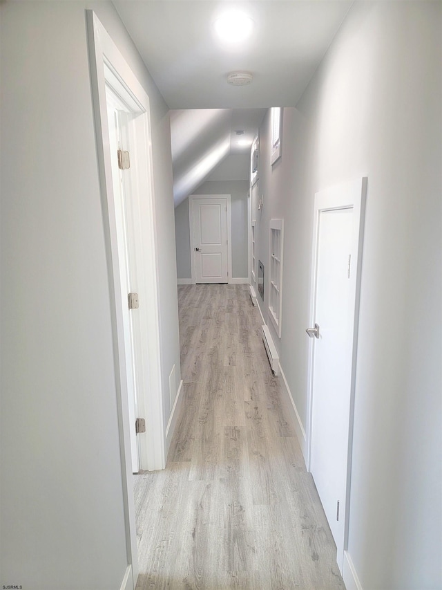 corridor featuring lofted ceiling, light wood-style flooring, a baseboard heating unit, and baseboards