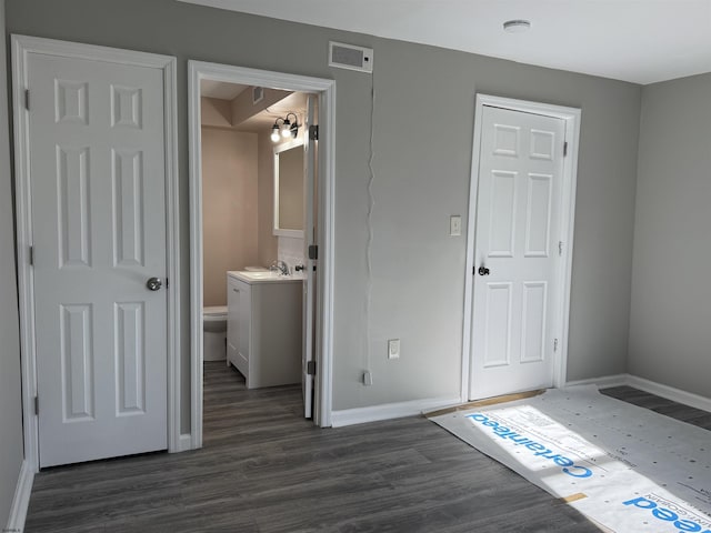 unfurnished bedroom featuring ensuite bathroom, a sink, visible vents, baseboards, and dark wood finished floors