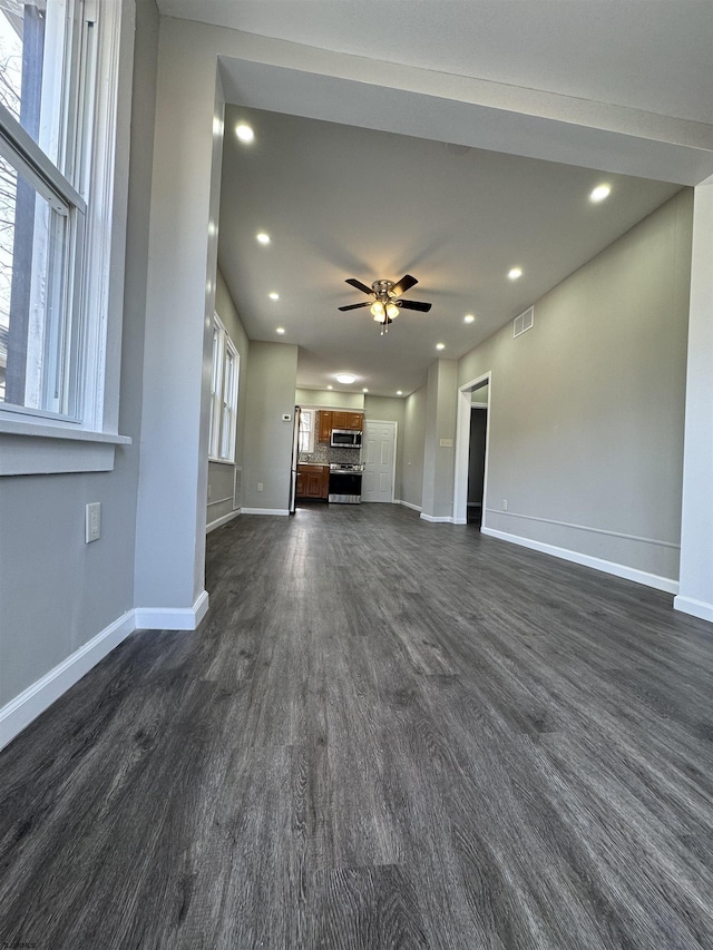 unfurnished living room with visible vents, baseboards, dark wood-style flooring, and a wealth of natural light