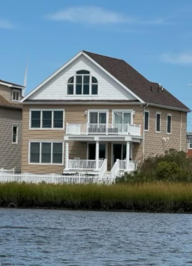 rear view of property with a balcony, a water view, and fence