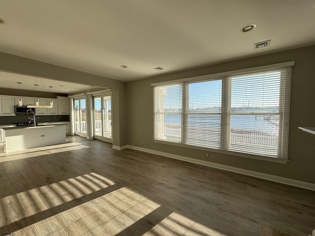 unfurnished living room with baseboards, visible vents, wood finished floors, a water view, and recessed lighting