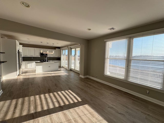 unfurnished living room featuring light wood-type flooring, visible vents, baseboards, and a sink