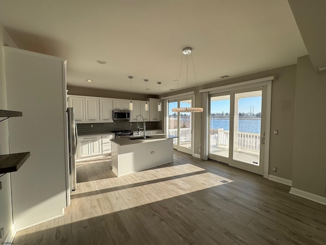 kitchen with a kitchen island with sink, a water view, white cabinetry, hanging light fixtures, and appliances with stainless steel finishes