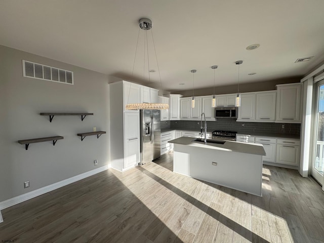 kitchen with visible vents, white cabinets, an island with sink, hanging light fixtures, and stainless steel appliances