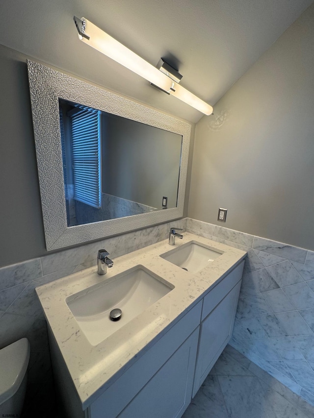 bathroom featuring marble finish floor, a sink, and tile walls