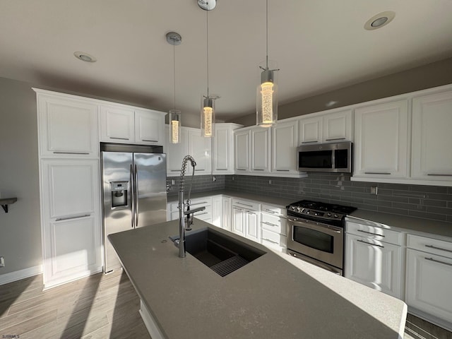 kitchen with appliances with stainless steel finishes, pendant lighting, white cabinetry, and a sink