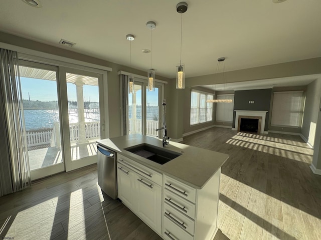 kitchen featuring dishwasher, hanging light fixtures, a water view, a kitchen island with sink, and white cabinetry