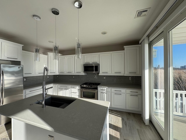 kitchen featuring white cabinetry, appliances with stainless steel finishes, a sink, and decorative light fixtures