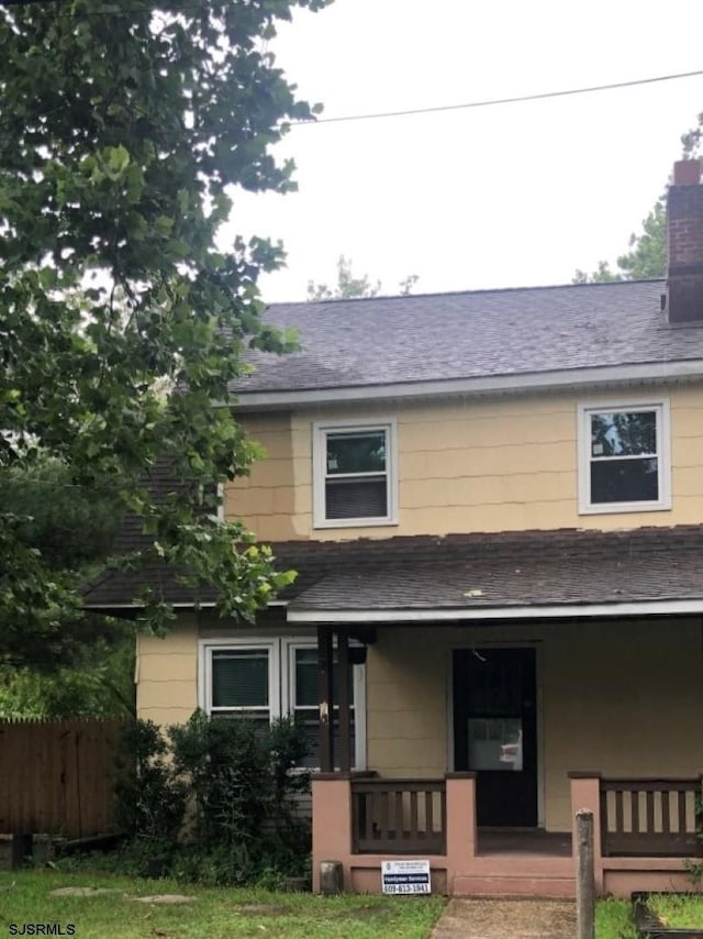 view of front of home featuring roof with shingles, a porch, a chimney, and fence