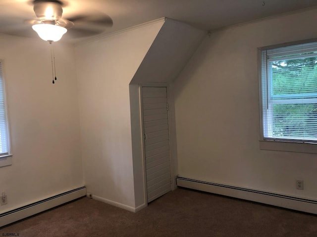 additional living space with a baseboard heating unit, dark carpet, a ceiling fan, and baseboards