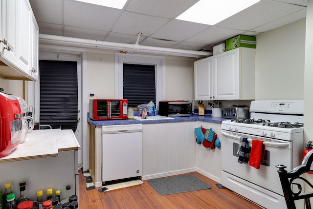 kitchen featuring a drop ceiling, white appliances, a sink, white cabinetry, and light wood-type flooring