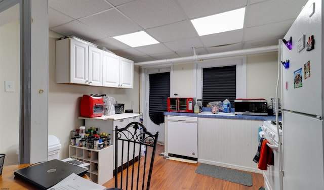 kitchen with light wood finished floors, a paneled ceiling, light countertops, white cabinets, and white appliances