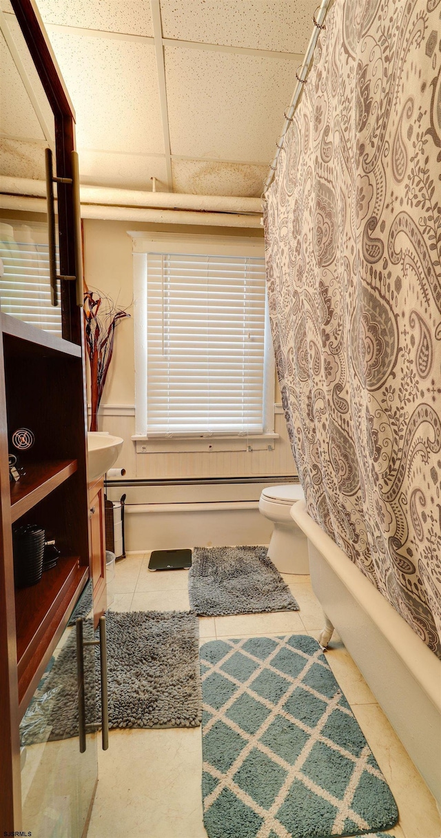 full bath with a wainscoted wall, toilet, shower / tub combo, tile patterned flooring, and a drop ceiling