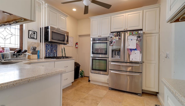 kitchen featuring tasteful backsplash, white cabinetry, stainless steel appliances, and light stone counters