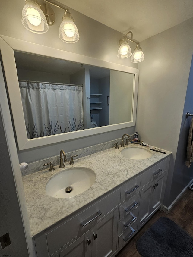 bathroom featuring double vanity, baseboards, a sink, and wood finished floors