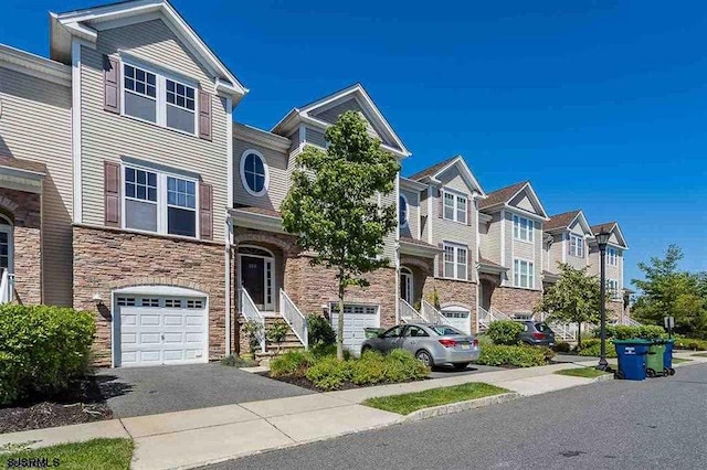 view of property with an attached garage, stone siding, a residential view, and aphalt driveway